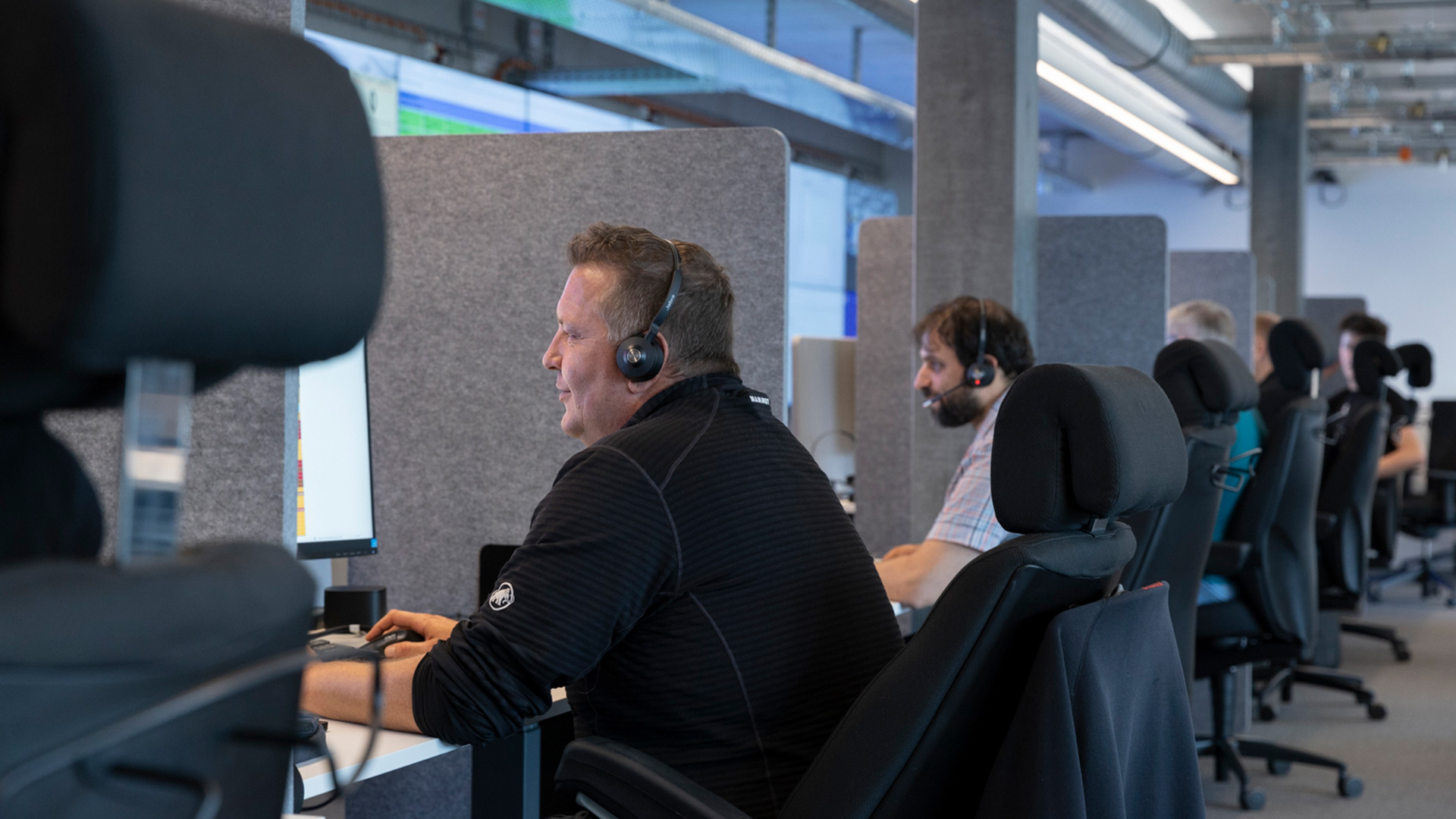 Mehrere Personen mit Headsets sitzen in einer Reihe vor ihren Bildschirmen.