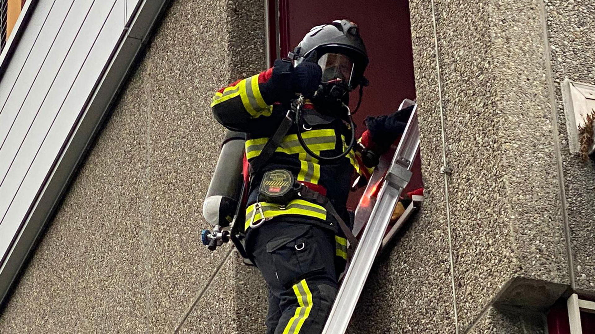 Timo Maibach steht auf einer Leiter, welche an ein Fenster gelehnt ist. Er trägt die volle Atemschutzausrüstung.