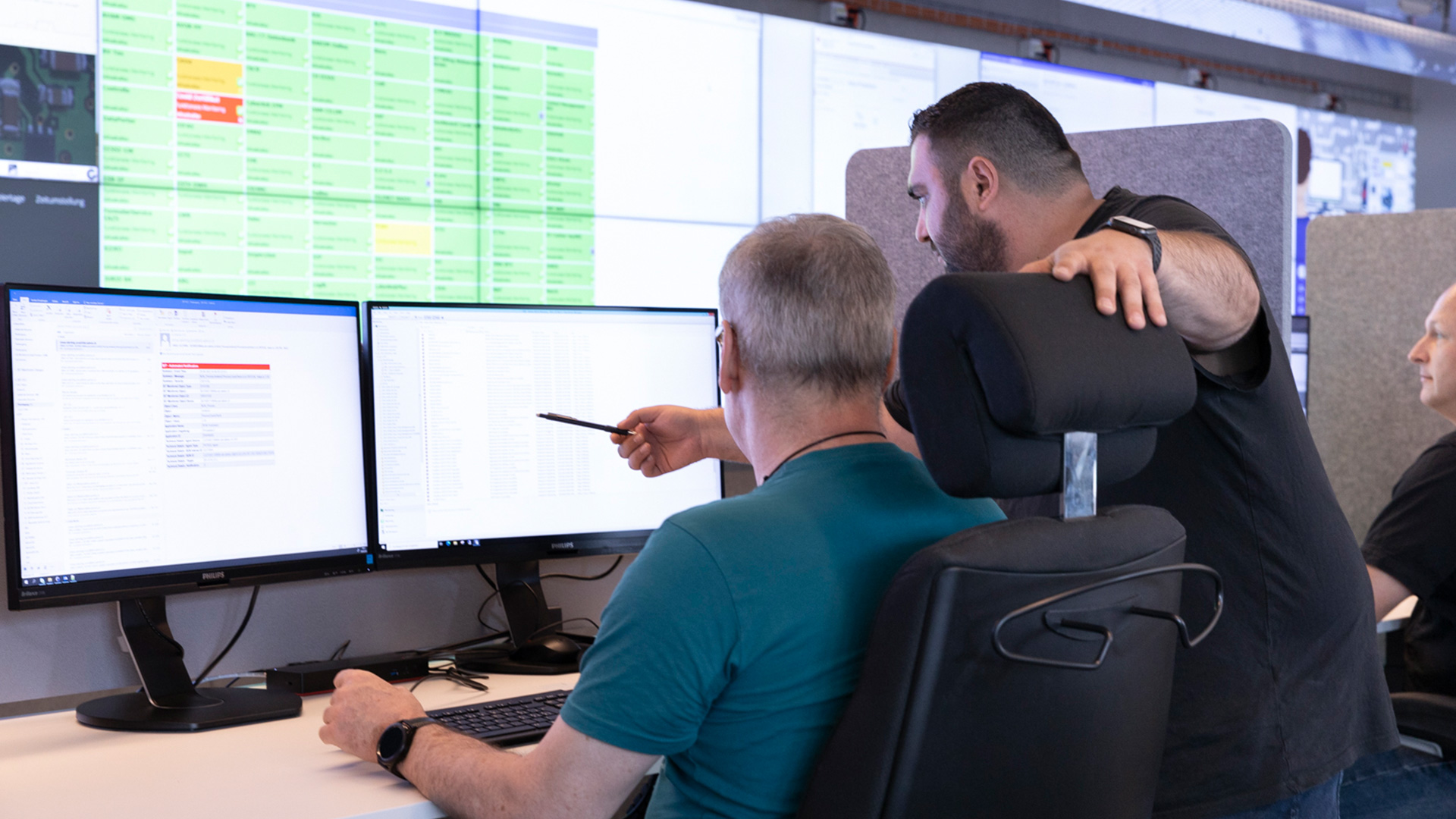 Une personne debout désigne quelque chose sur un écran à l’attention d’une deuxième personne assise.