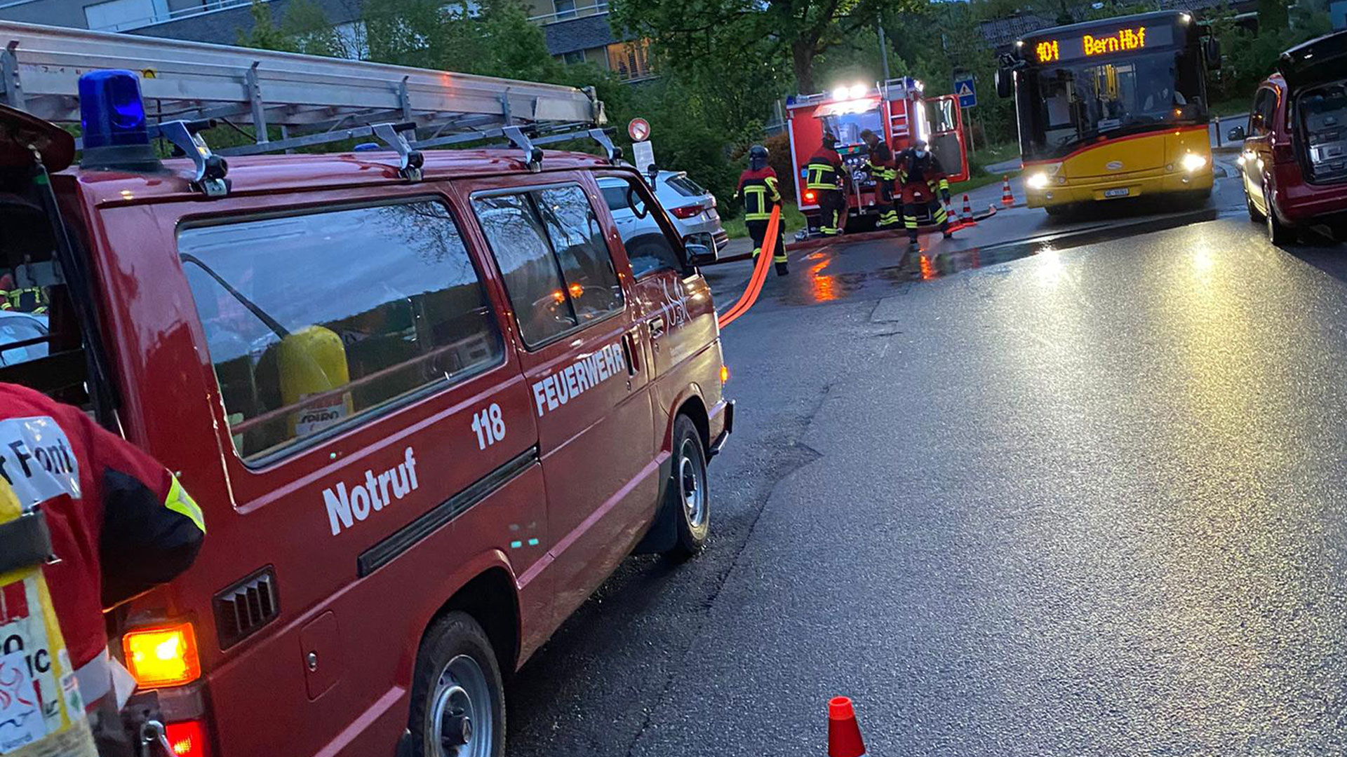 Après l'extinction d'un incendie, de nombreux sapeurs-pompiers chargent dans deux camions le matériel qu'ils ont utilisé. Un bus passe.